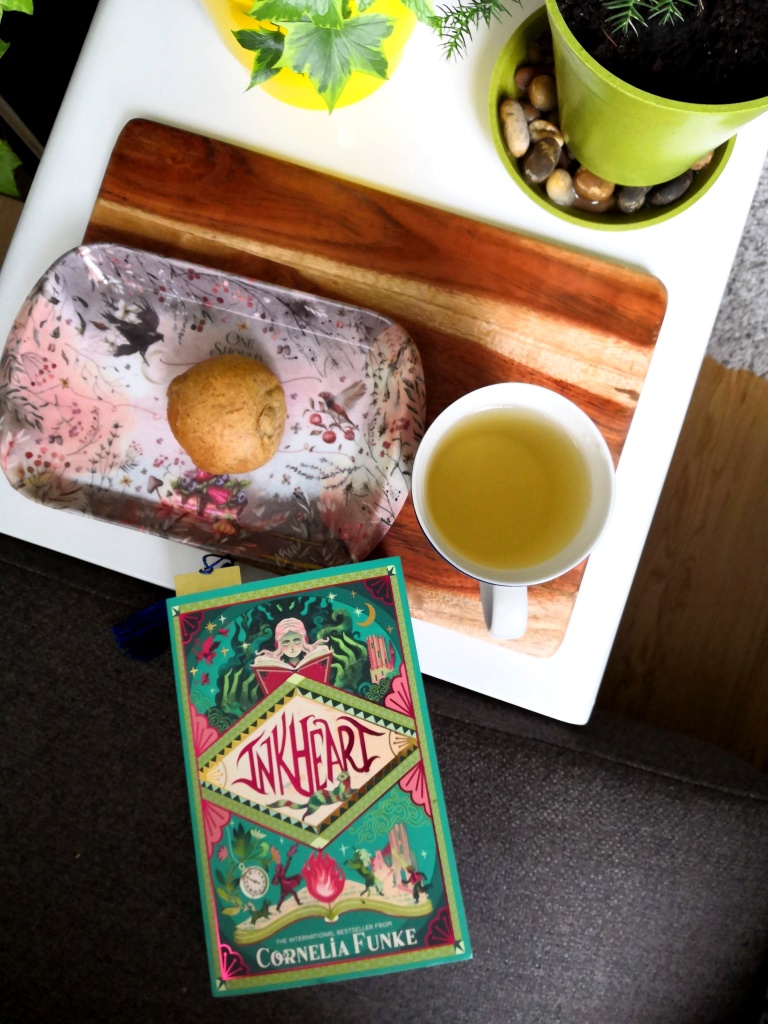 Picture of Inkheart, a raisin-bun and green tea on a small table next to a couch.
