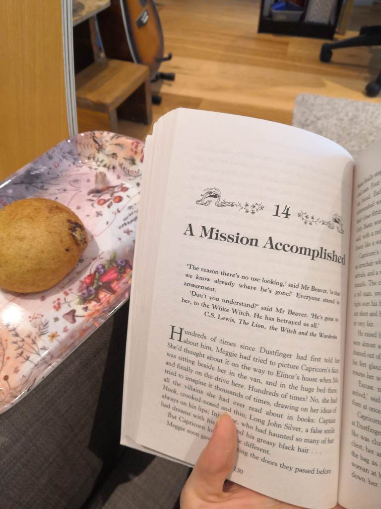 A picture of Inkheart chapter 14, page 130. A raisin-bun is next to the book on a pink, patterned cake tray.
