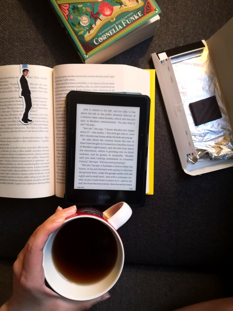 A picture of an open book (Finnish edition of A Little Life), the ebook version of A Little Life, Inkheart, dark chocolate and a cup of tea with my hands wrapped around the mug.