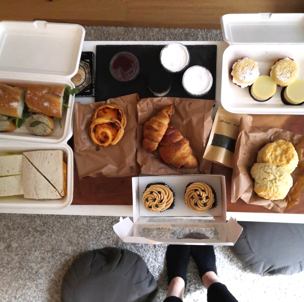 A picture of a table full of food; sandwiches, baquettes, cupcakes, croissants, tea, scones, cakes etc